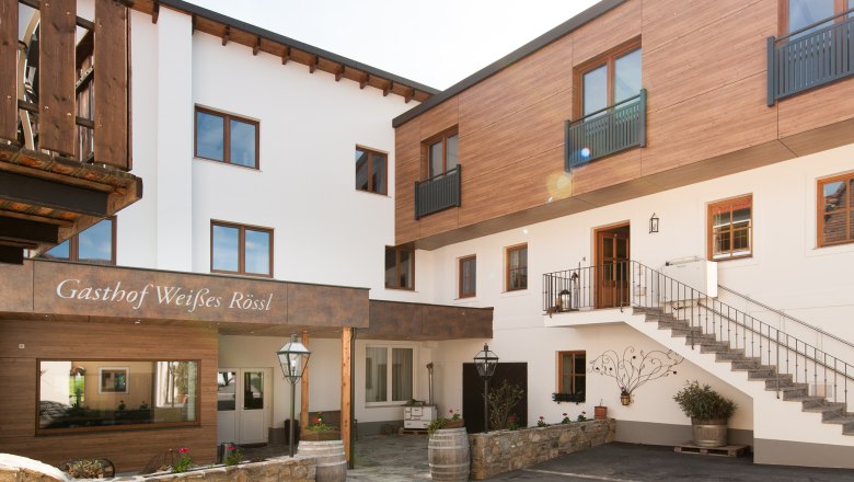 Außenansicht eines Gasthofs mit Holz- und weißen Fassaden, Treppe und Dekorationen.