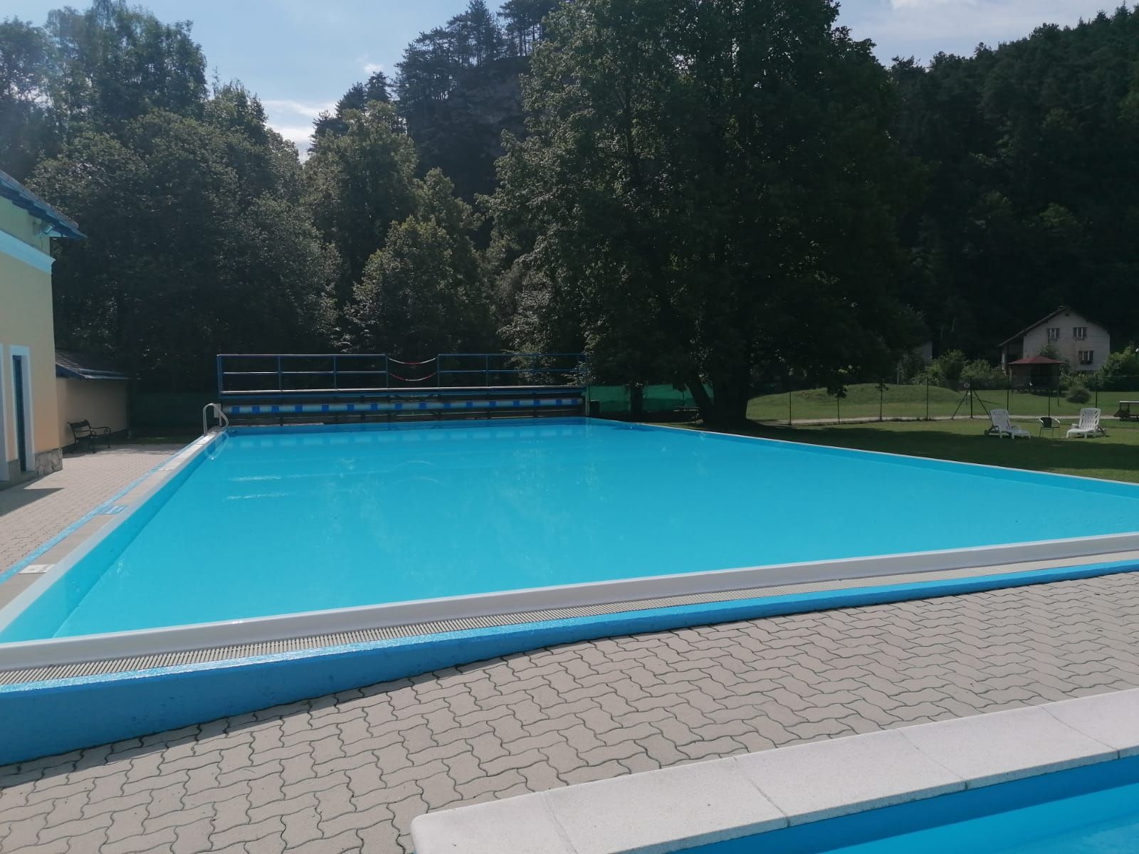 Ein leerer Swimmingpool im Freien, umgeben von Bäumen und einem Gebäude.