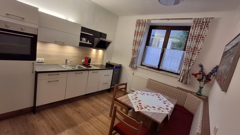 Moderne K&uuml;che mit Eckbank, Tisch und Fenster mit Vorh&auml;ngen.