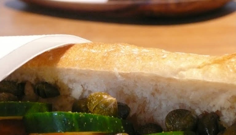 Nahaufnahme eines belegten Sandwiches mit Gurken, Tomaten und Kapern.