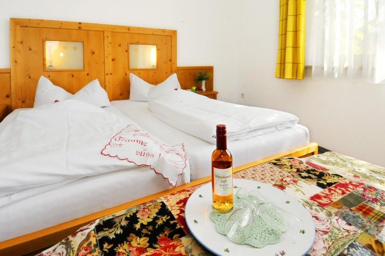 Gemütliches Hotelzimmer mit Doppelbett, dekoriert mit einem bestickten Kissen und einer Flasche Wein auf einem Tisch.