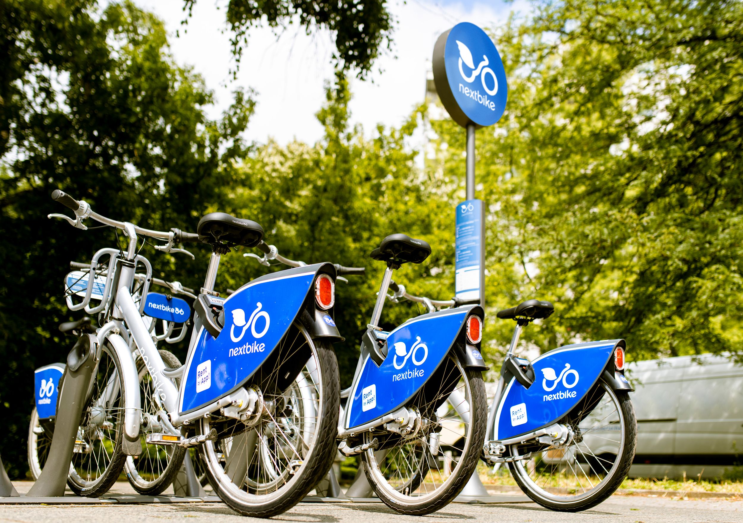 Mehrere Nextbike-Fahrräder an einer Station im Freien, umgeben von Bäumen.