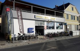 Fahrradgeschäft mit Fahrrädern vor dem Gebäude und Werbefahnen.