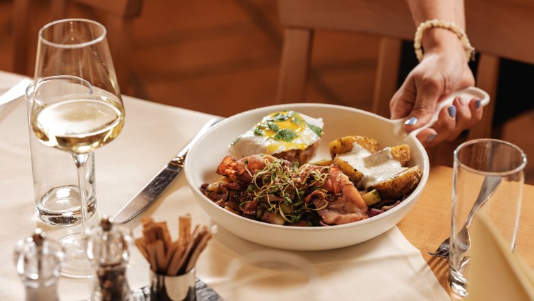 Ein Teller mit Essen und ein Glas Weißwein auf einem gedeckten Tisch.