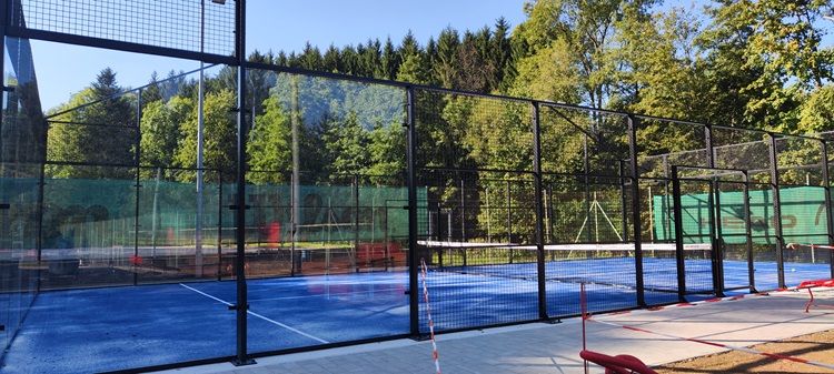 Padeltennisplatz in Bad Schönau mit blauem Boden und umliegendem Wald.