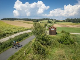 Die sanften Hügel und weitläufigen Felder laden zu einer erfrischenden Radtour ein. Radfahrer genießen die idyllische Landschaft, während die Sonne über den Horizont strahlt und die Wolken sanft am Himmel treiben. Ein perfekter Tag, um die Natur in ihrer vollen Pracht zu erleben.