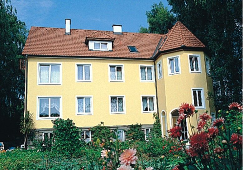 Gelbes Haus mit rotem Dach und Garten im Vordergrund.