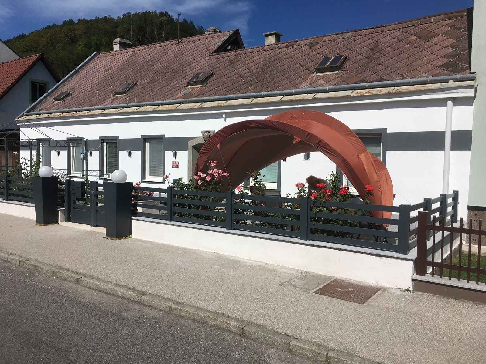 Ein weißes Haus mit einem kleinen Garten und einem orangefarbenen Pavillon vor der Tür.