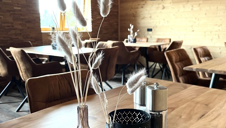 Gemütlicher Raum aus Holz, Dekoration auf Holztisch, Schriftzug 'dahoam' an der Wand.