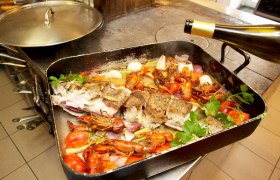 Ein Bräter mit Fisch, Flusskrebsen, Gemüse und Kräutern auf einem Herd.