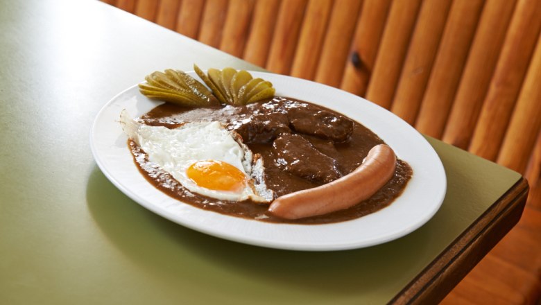 Ein Teller mit Bratensauce, Spiegelei, Wurst und Gurkenscheiben.