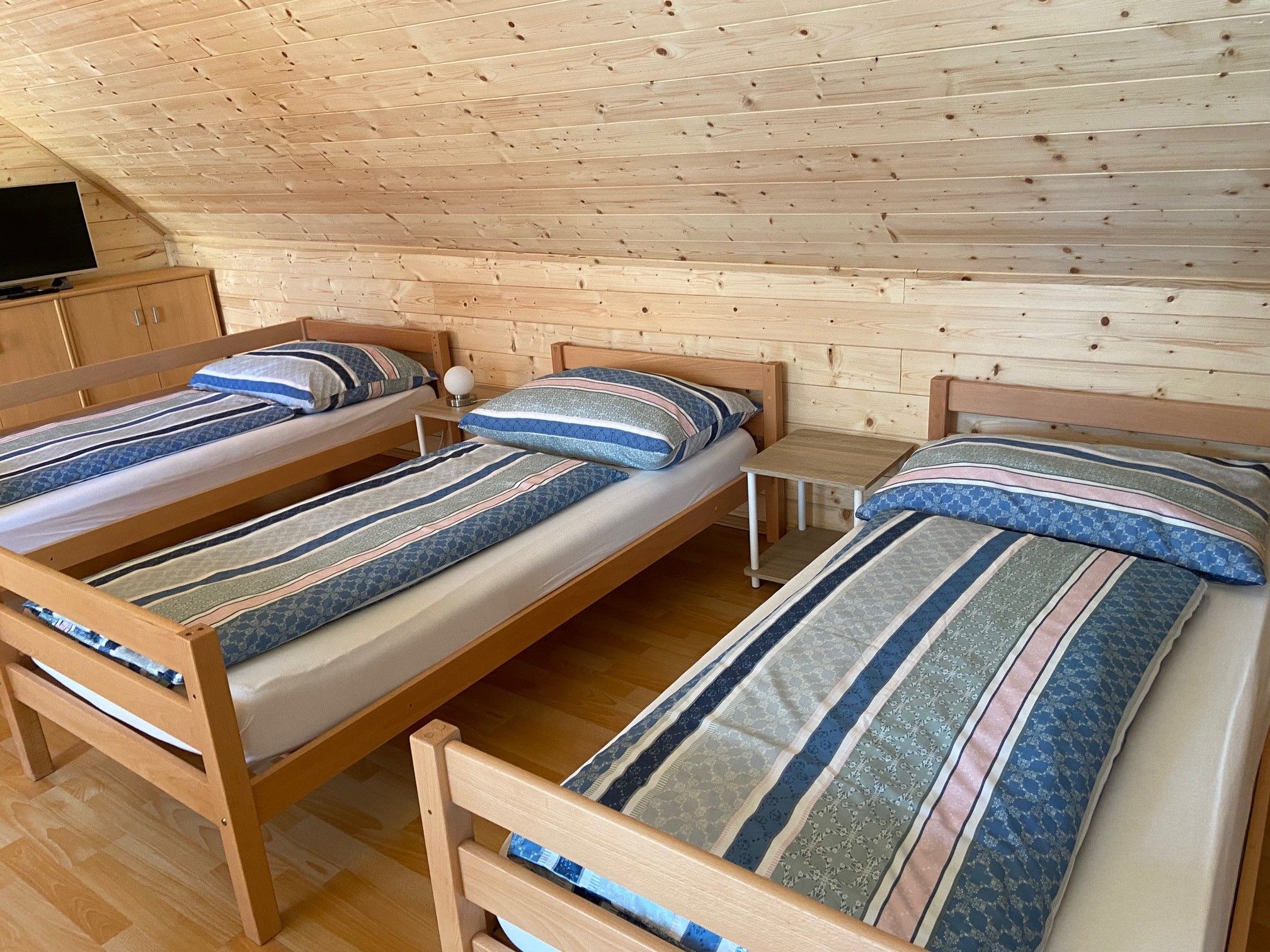 Drei Einzelbetten in einem Zimmer mit Holzverkleidung und einem Fernseher.