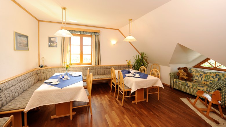 Gem&uuml;tlicher Fr&uuml;hst&uuml;cksbereich mit Holzm&ouml;beln, gedeckten Tischen und einem Sofa mit Teddyb&auml;ren.