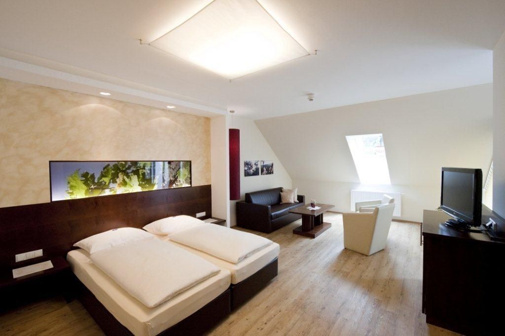 Modern eingerichtetes Hotelzimmer mit Doppelbett, Sofa, Sessel und Fernseher.