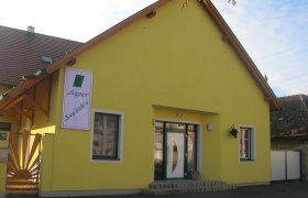 Gelbes Gebäude mit einem Schild "Aigner Ausg'steckt is" an der Fassade.
