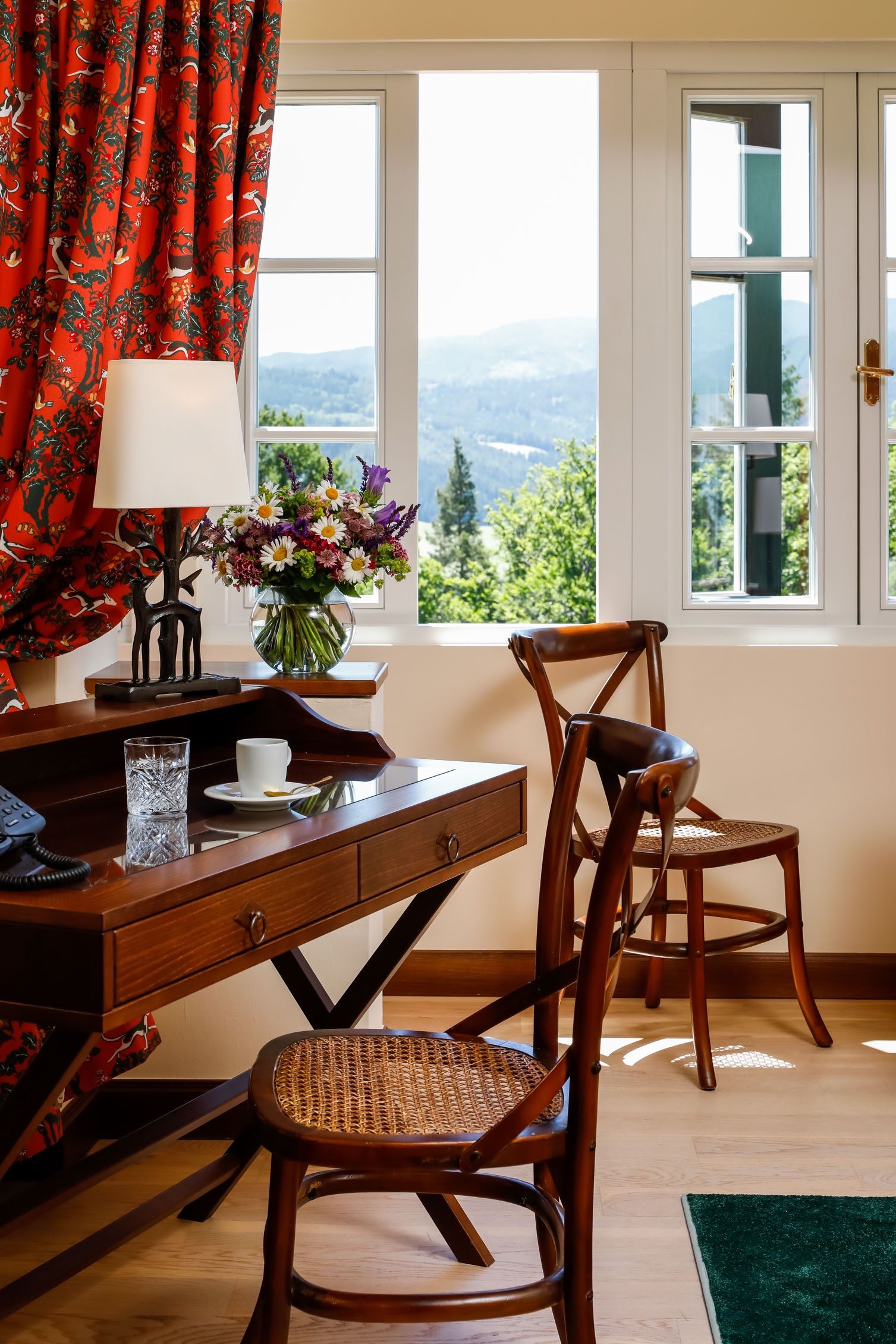 Ein elegantes Zimmer mit Holzmöbeln, einem Schreibtisch, Stühlen und einem Fenster mit Blick auf eine grüne Landschaft.