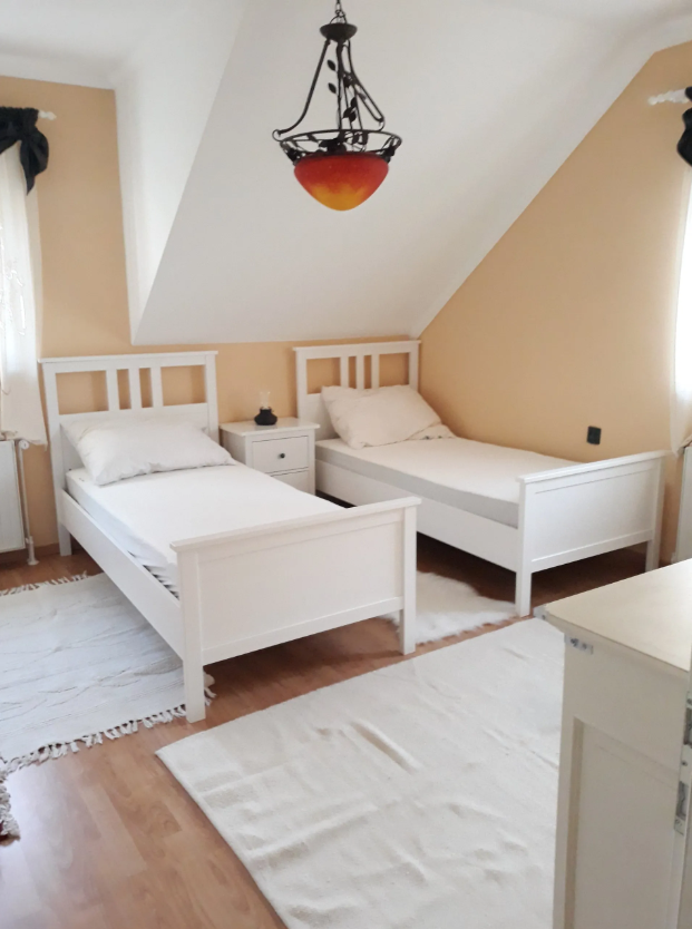 Schlafzimmer mit zwei weißen Einzelbetten und einem Nachttisch dazwischen.
