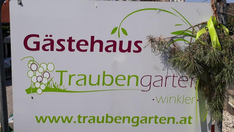 Schild mit der Aufschrift 'G&auml;stehaus Traubengarten Winkler' und Website-Adresse, dekoriert mit Zweigen.