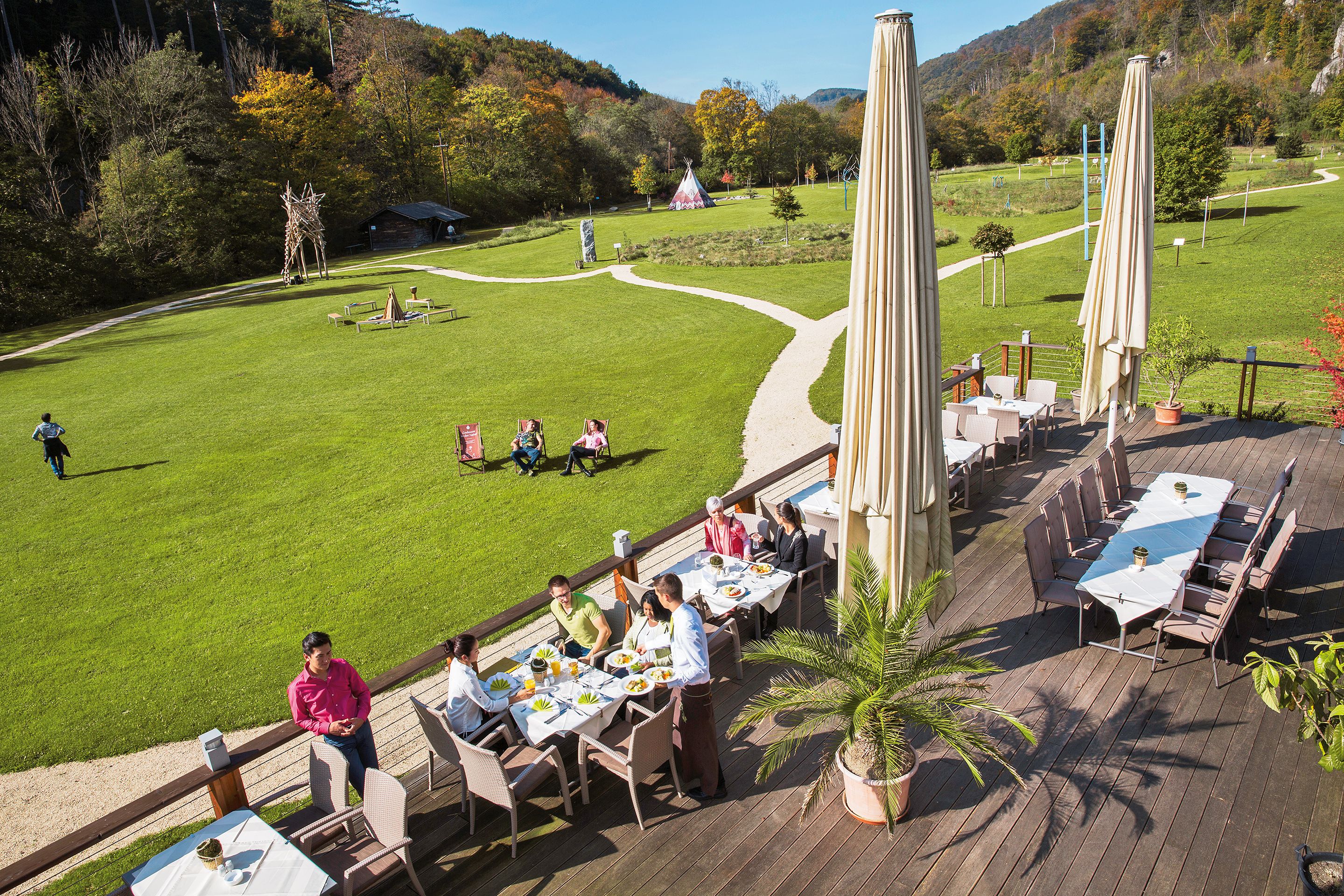 Terrasse des Seminar- und Eventhotels Krainerhütte mit Gästen beim Essen, umgeben von grüner Wiese und Wald.