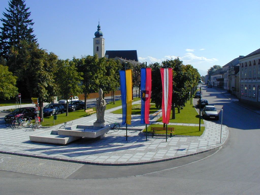 Platz in Ruprechtshofen mit Kirche, Statuen und Fahnen.