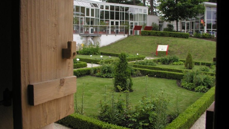 Ein gepflegter Garten mit Hecken und Pflanzen, umgeben von modernen Geb&auml;uden mit Glasfassaden.