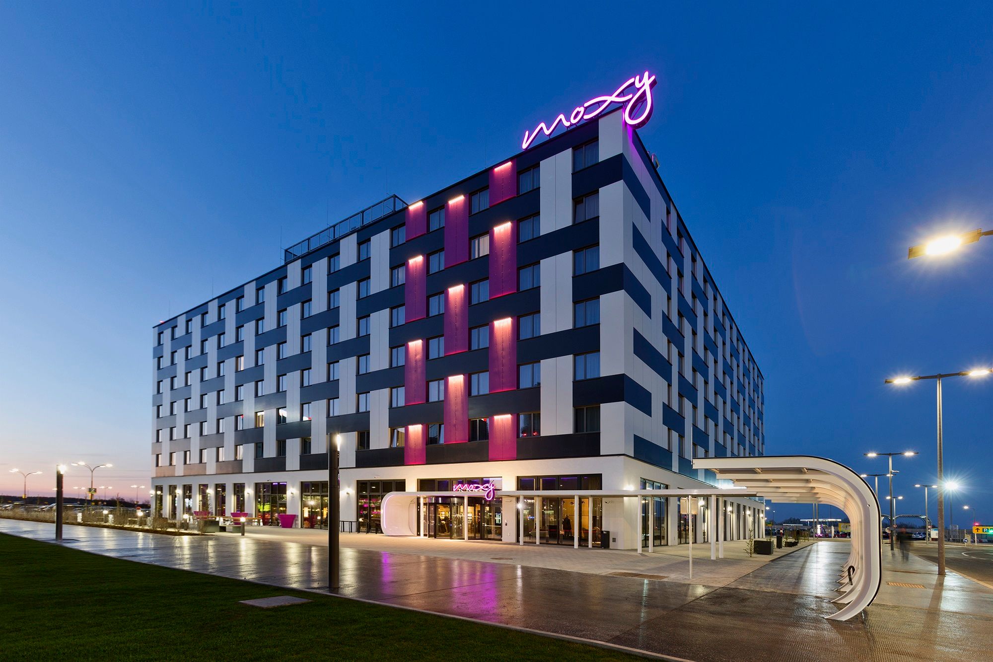 Außenansicht des Moxy Vienna Airport Hotels bei Dämmerung mit beleuchtetem Schriftzug.