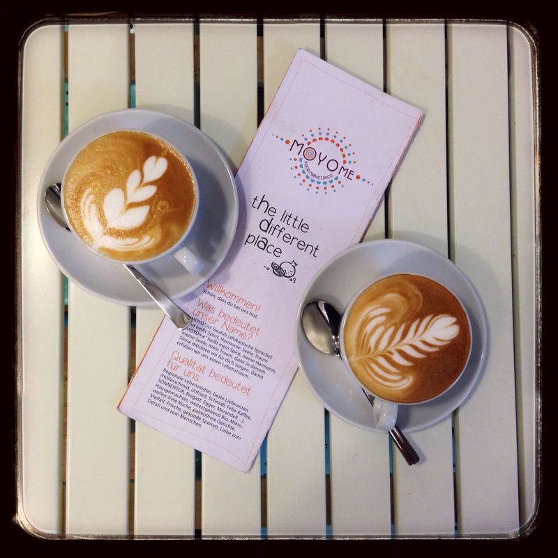 Zwei Cappuccinos mit Latte Art und ein Flyer auf einem Tisch.