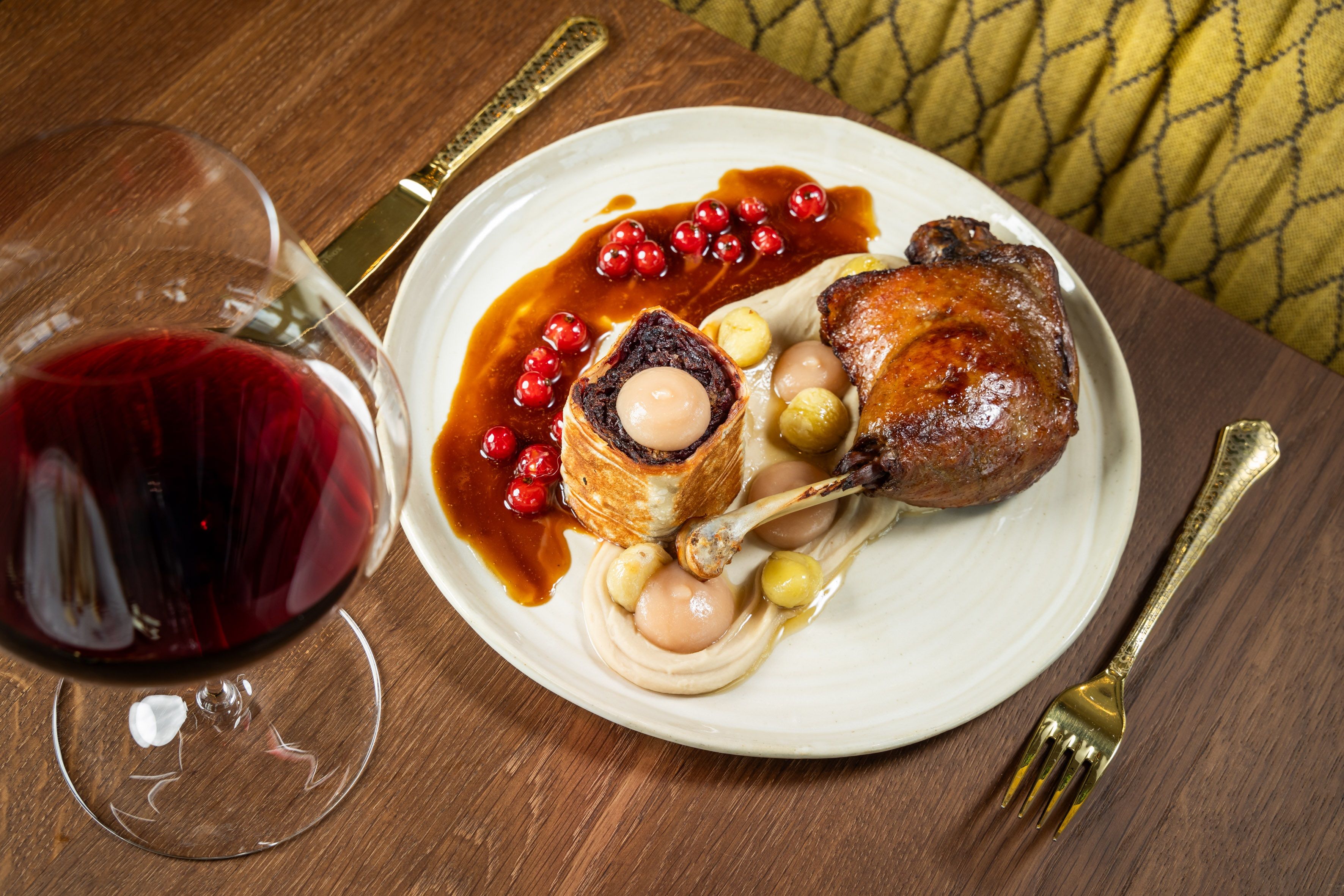 Ein Teller mit Gänsekeule, Beilagen und Rotwein auf einem Holztisch.