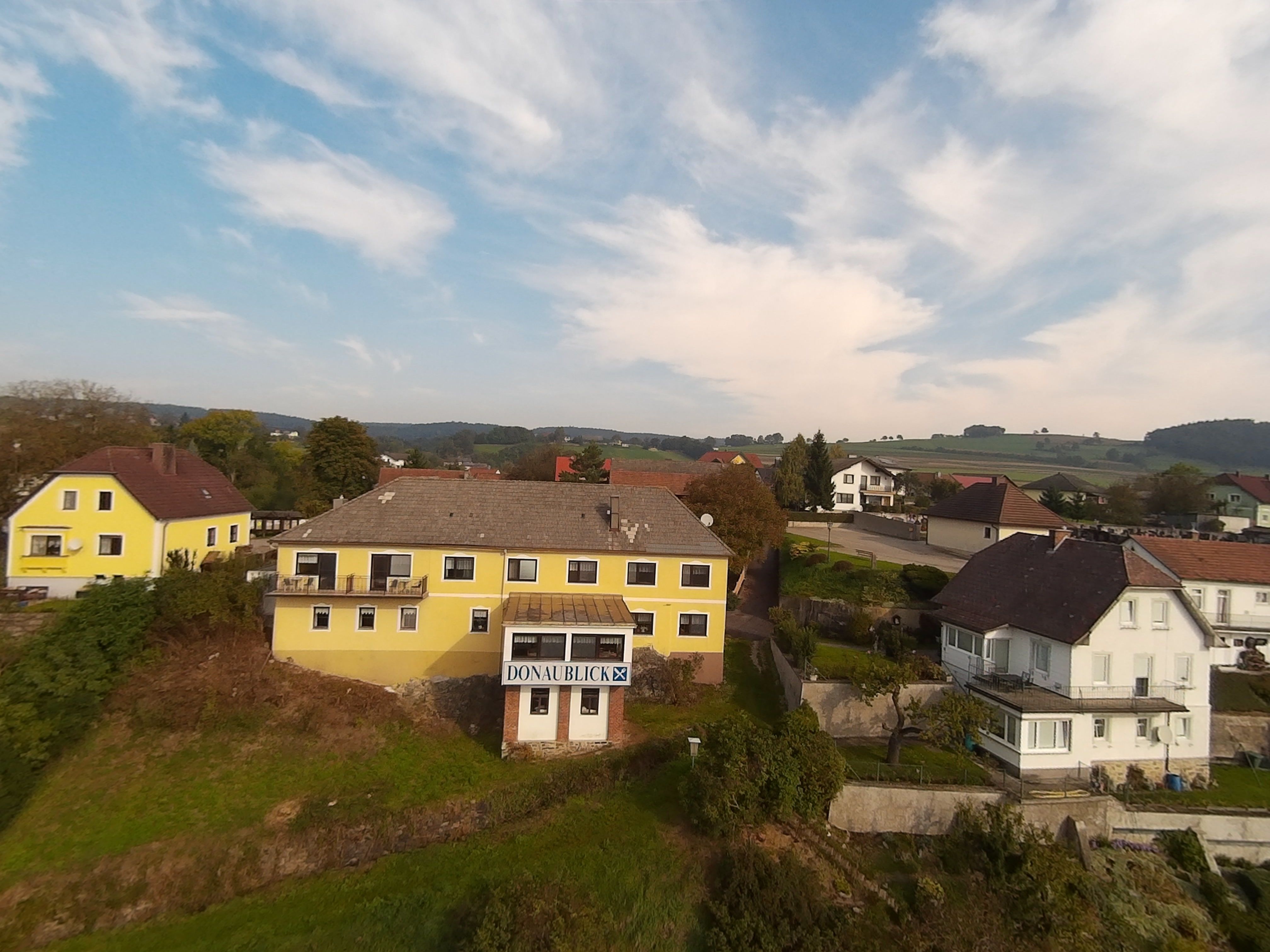 Landschaft mit gelben und weißen Häusern, blauer Himmel, Hügel im Hintergrund.