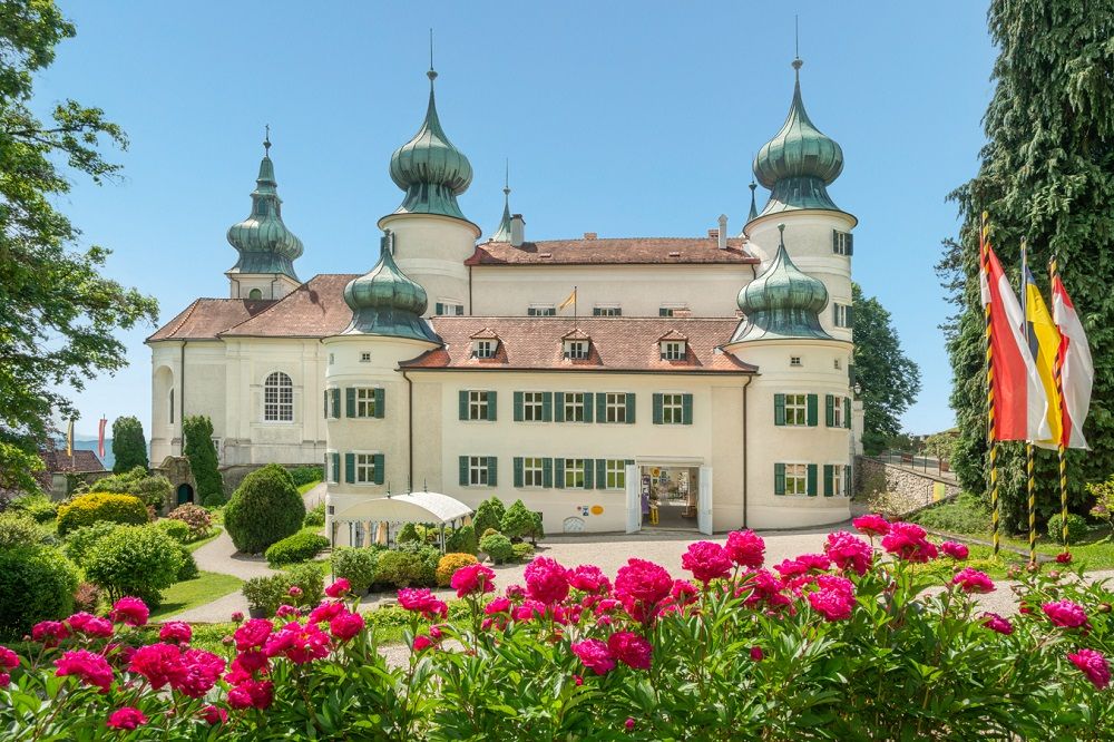 Schloss Artstetten mit blühenden Blumen im Vordergrund und Flaggen rechts.