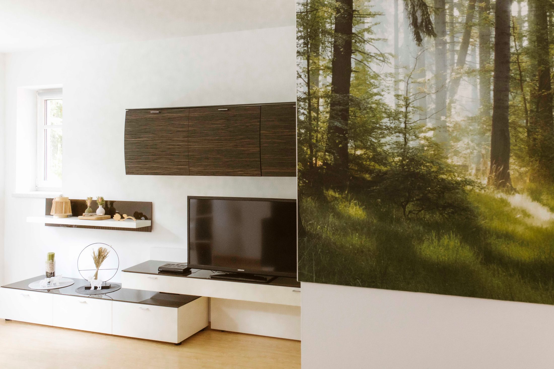 Moderner Wohnbereich mit TV, Regalen und großem Waldbild an der Wand.