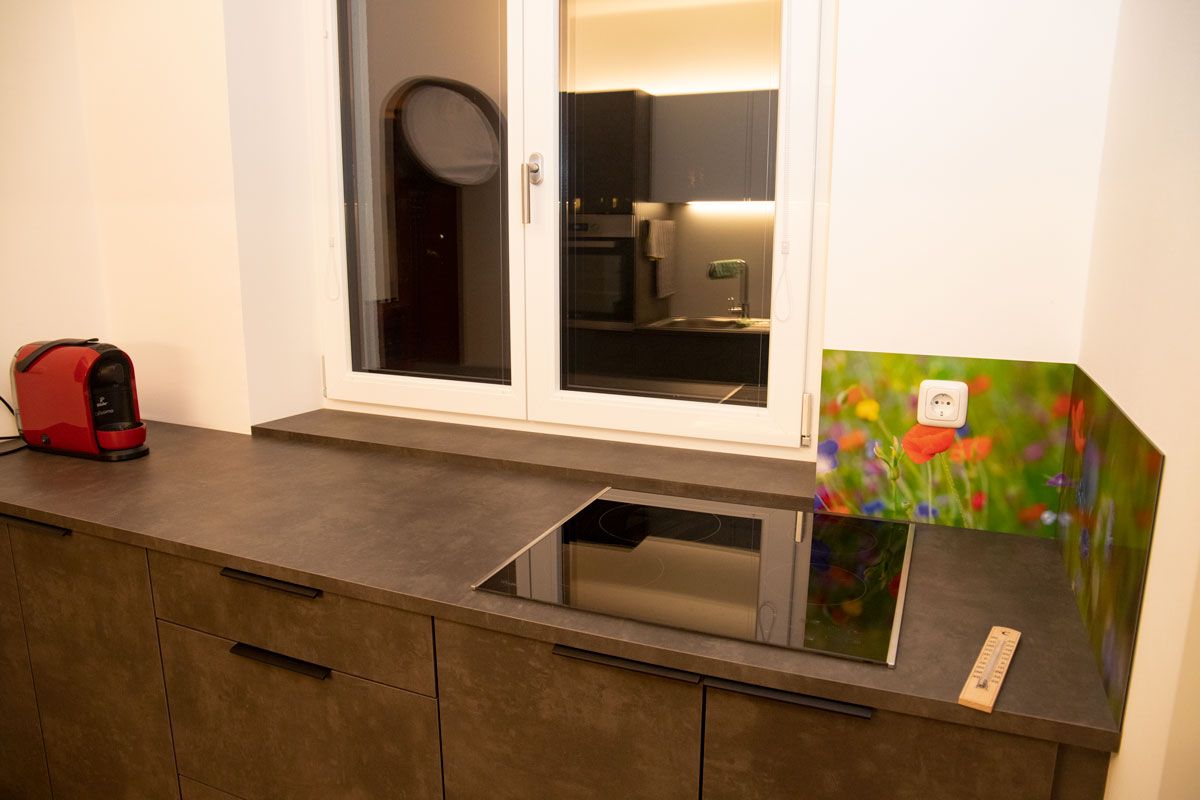 Moderne Küche mit Induktionskochfeld, roter Kaffeemaschine und bunter Blumenrückwand.