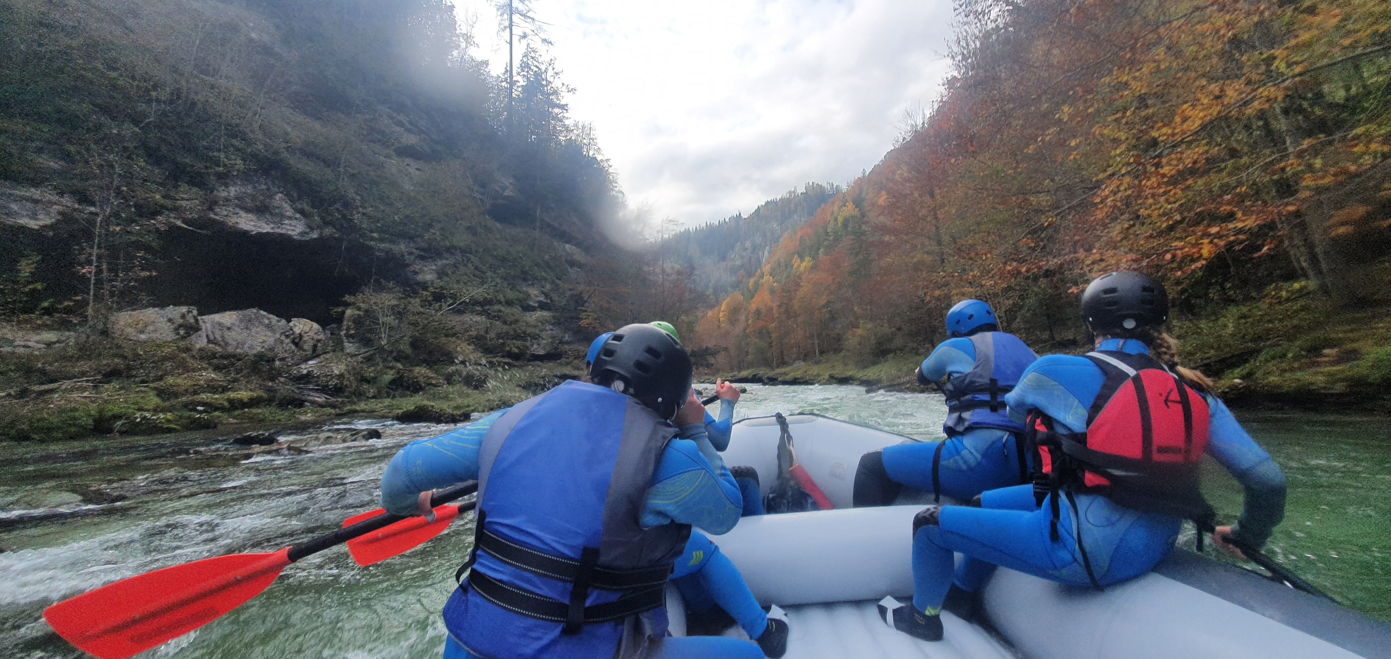 Gruppe beim Rafting auf einem Fluss, umgeben von herbstlichen Bäumen.