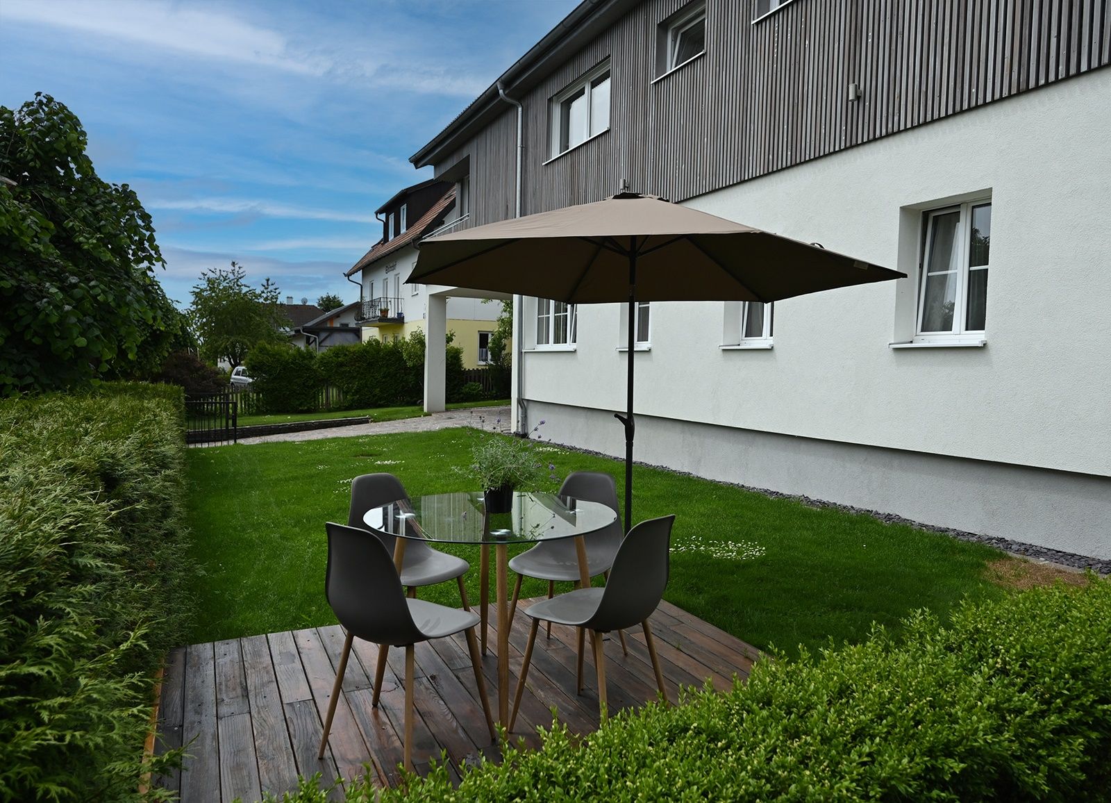 Garten mit Sitzbereich, Tisch, Stühlen und Sonnenschirm auf Holzterrasse.