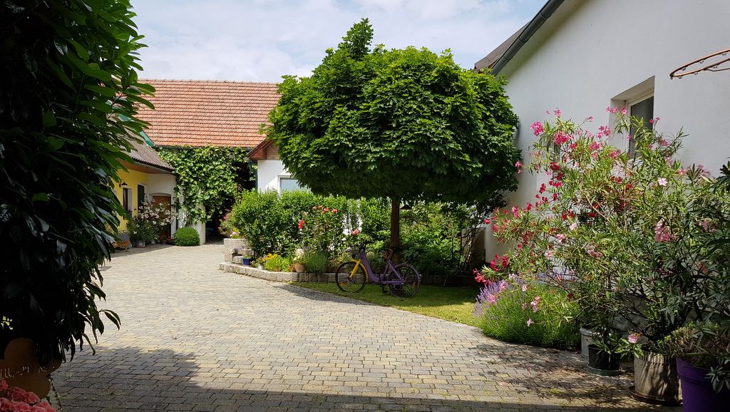 Innenhof mit gepflastertem Weg, Bäumen und blühenden Pflanzen.