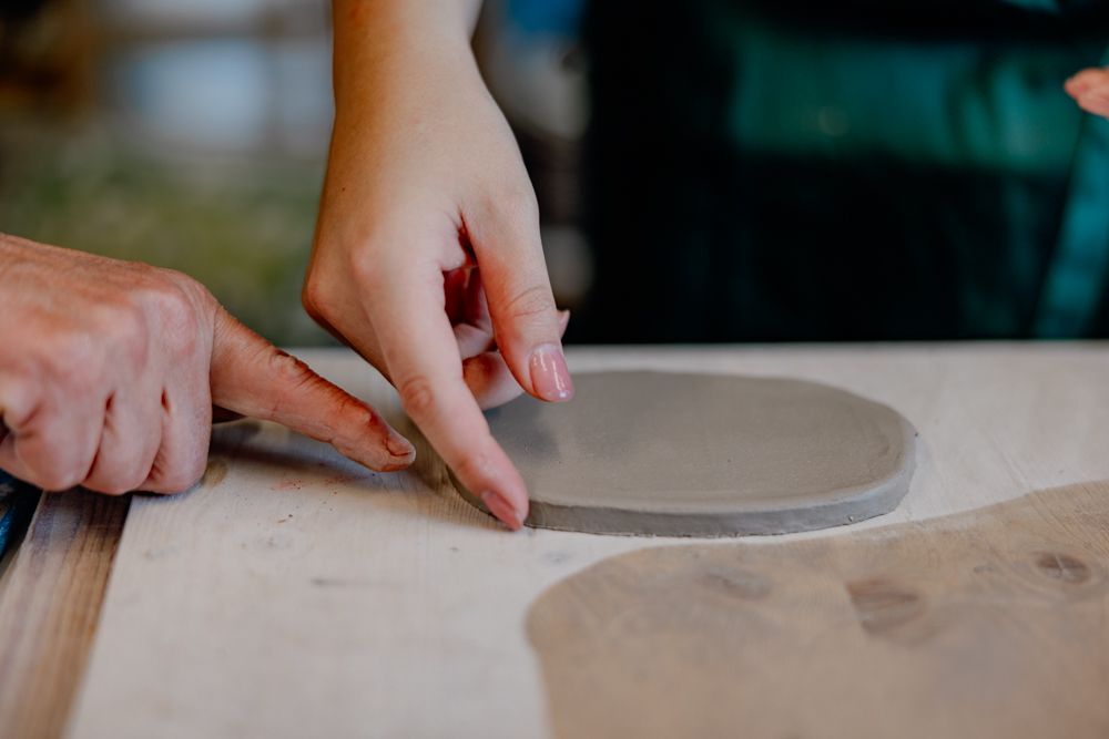 Zwei Hände formen Ton auf einem Tisch.