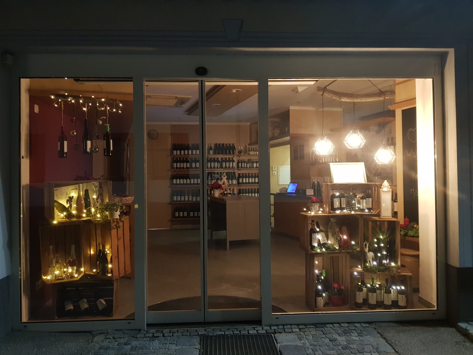 Weinladen bei Nacht mit beleuchtetem Schaufenster und Weinflaschen.