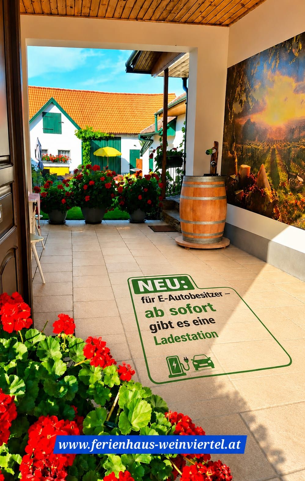 Innenhof eines Ferienhauses mit Blumen, Weinfass und Hinweis auf eine Ladestation für E-Autos; im Hintergrund ein Haus mit orangefarbenem Dach.