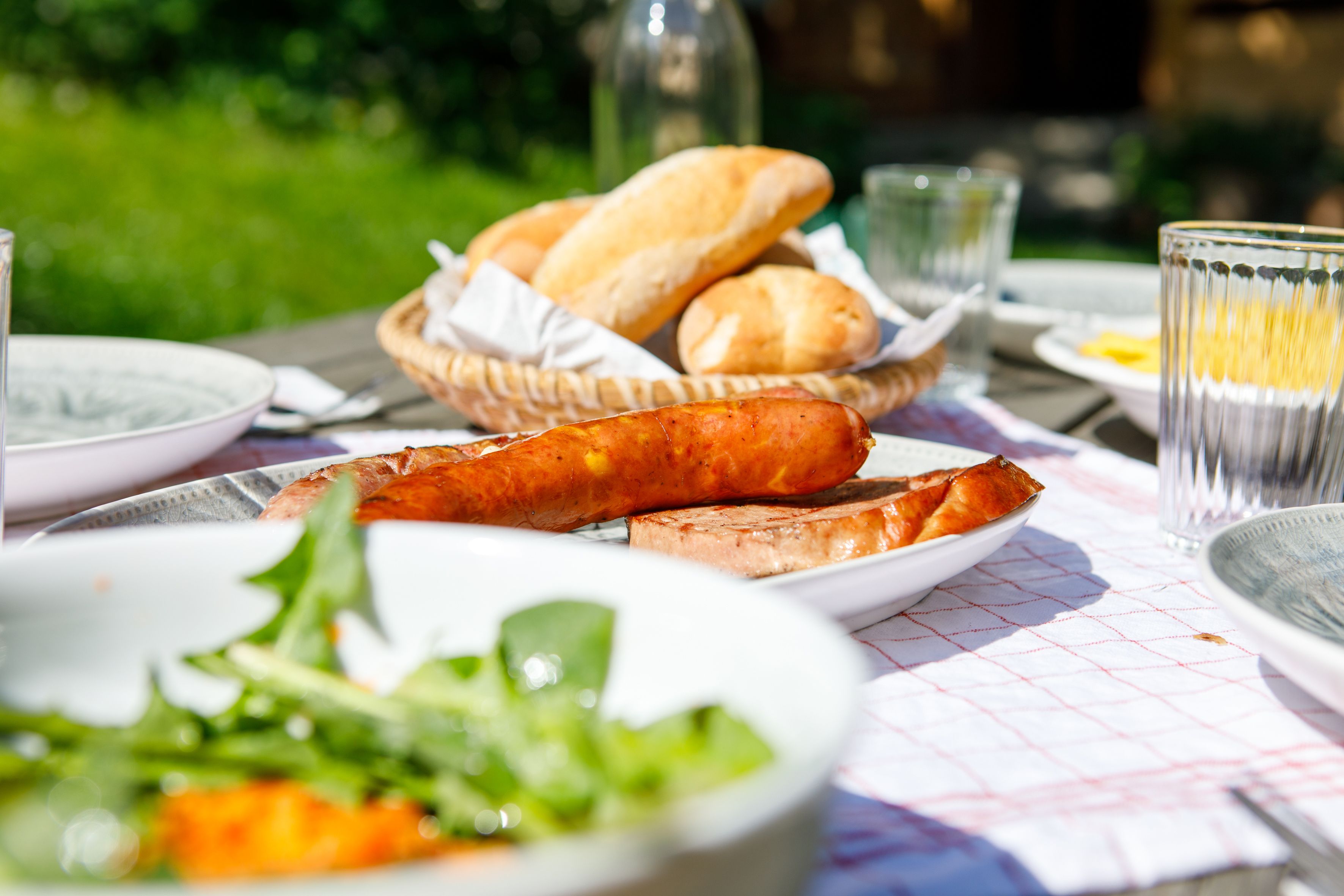 Ein Tisch im Freien mit Wurst, Brot und Salat, ideal für eine Sommerjause.