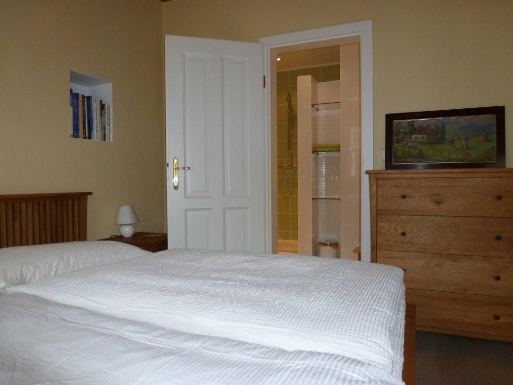 Ein gemütliches Doppelzimmer mit Bett, Kommode, Bücherregal und offenem Bad.