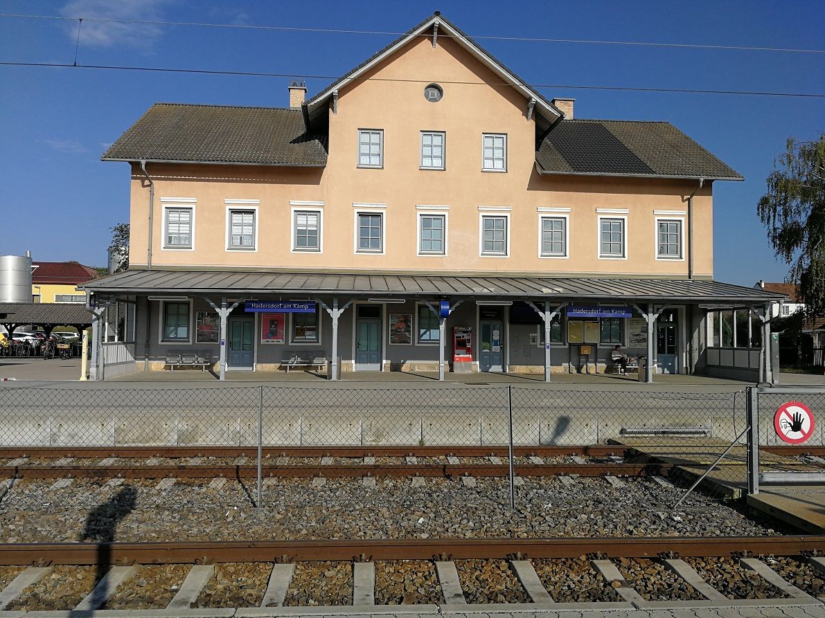 Bahnhof Hadersdorf am Kamp mit Gleisen im Vordergrund und einem gelben Gebäude im Hintergrund.
