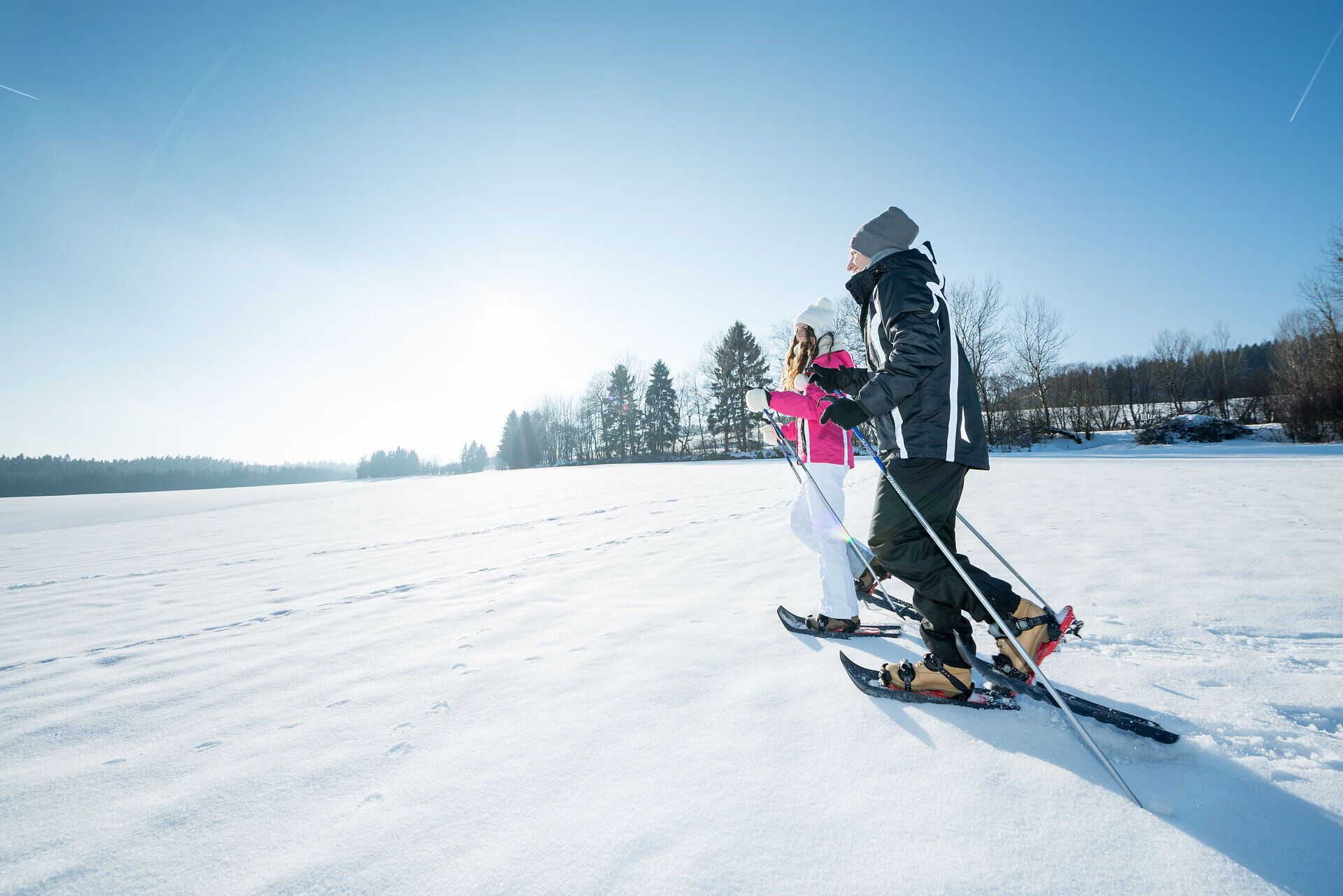 Zwei Personen beim Schneeschuhwandern auf einem verschneiten Feld unter klarem Himmel.