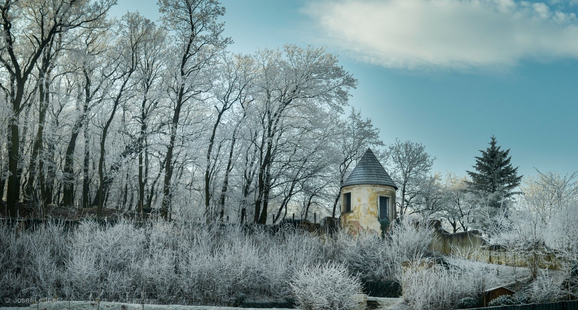 Ein alter Turm steht in einer verschneiten Landschaft, umgeben von Bäumen mit Raureif.