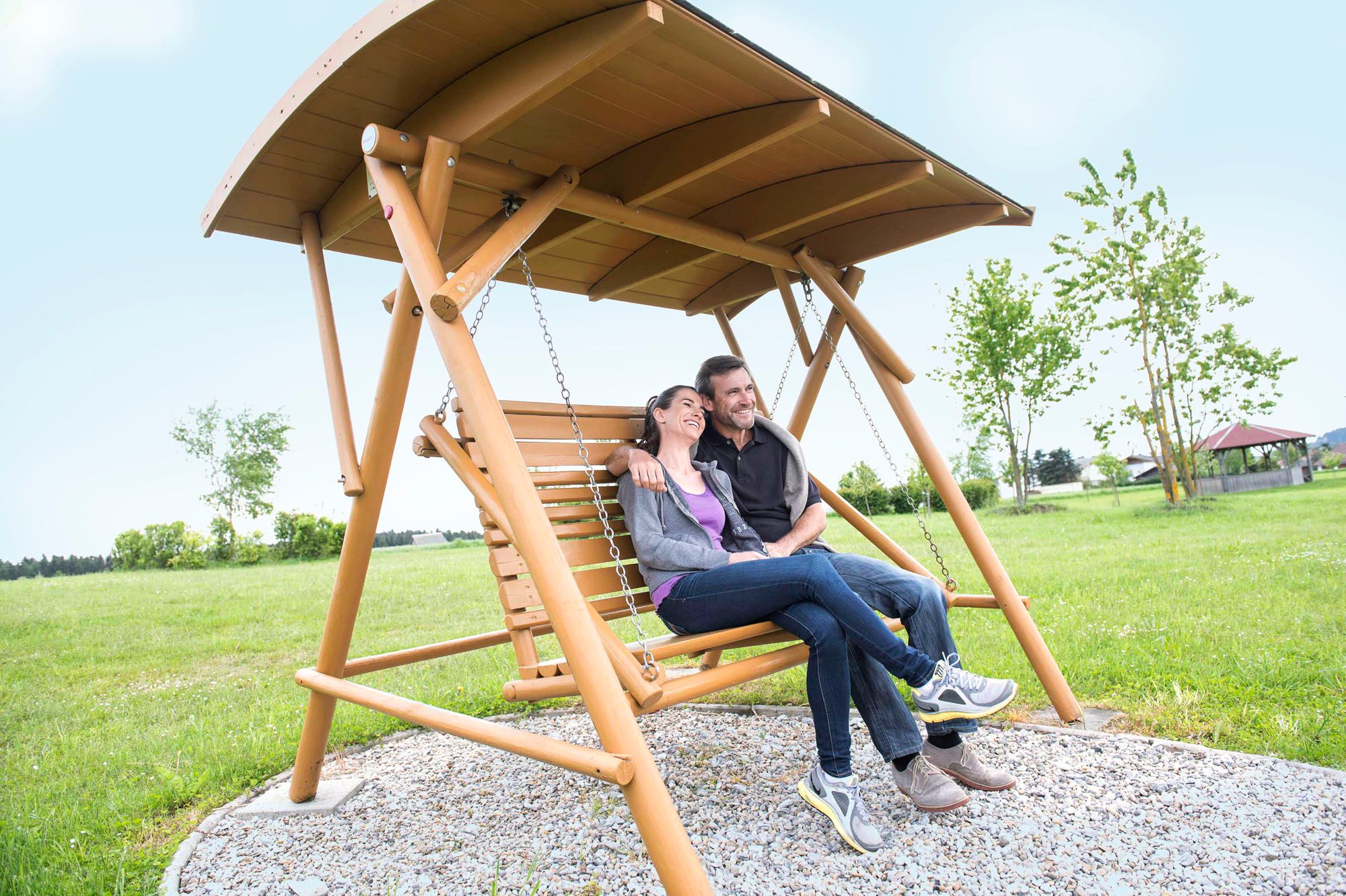 Ein Paar sitzt entspannt auf einer Holzschaukel im Freien.
