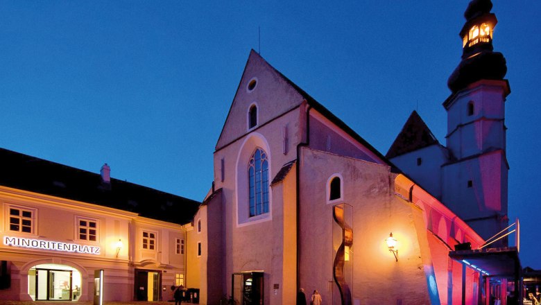 Außenansicht der beleuchteten Minoritenkirche in Krems bei Nacht.