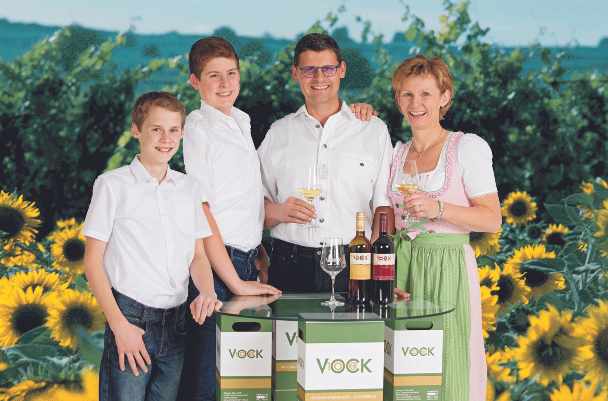 Familie mit Weinflaschen und Sonnenblumen im Hintergrund.