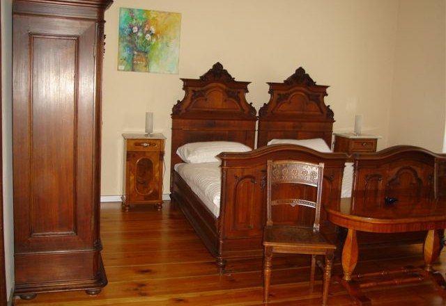 Ein traditionell eingerichtetes Schlafzimmer mit antiken Holzm&ouml;beln, darunter zwei Betten, ein Schrank und ein Tisch.