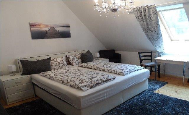 Doppelzimmer Ried Goissenberg, © Familie Denk Gemütliches Doppelzimmer mit Bett, Nachttischen, Tisch und Stühlen, dekoriert mit einem Bild und einem Kronleuchter.