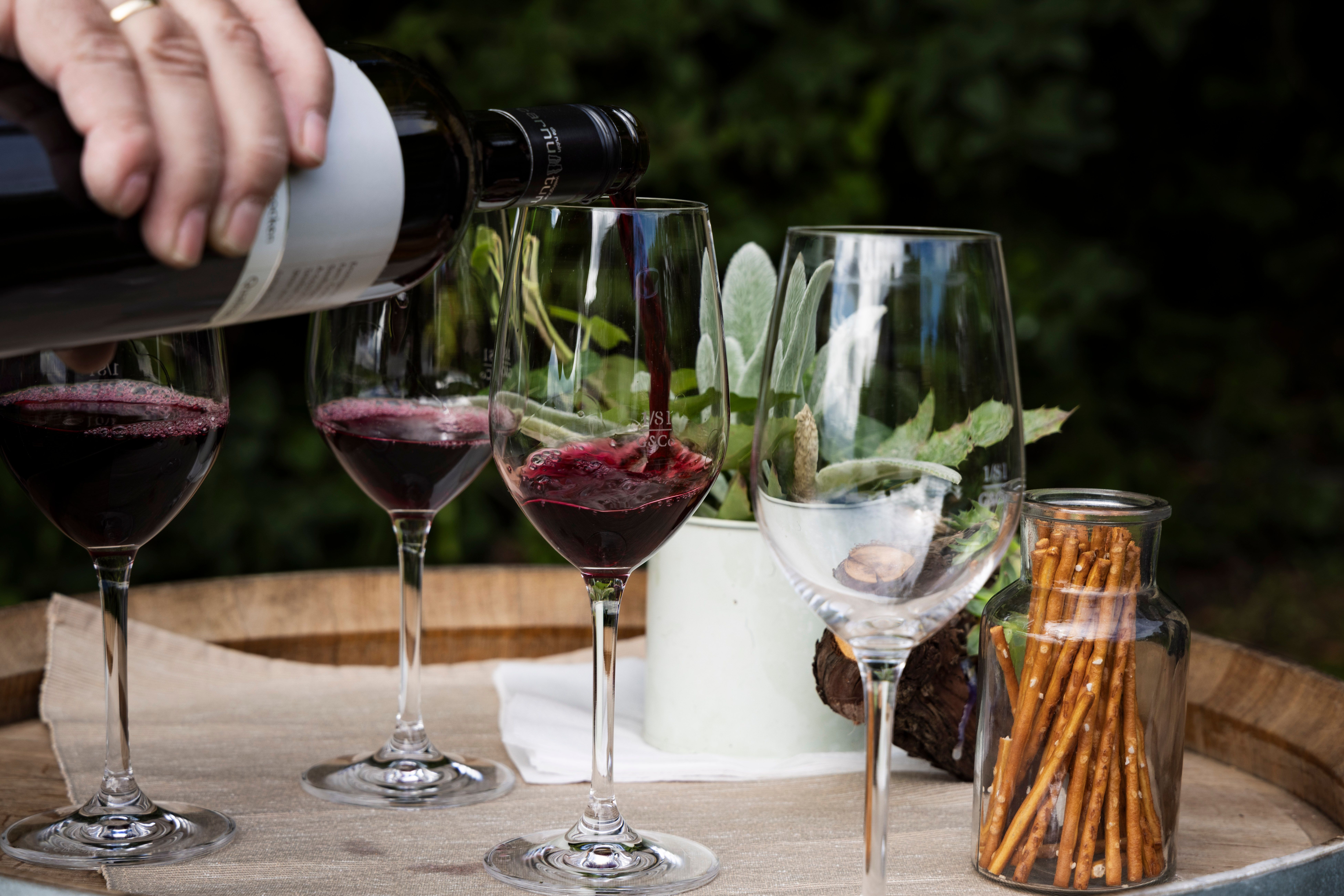 Hand gießt Rotwein in Gläser 