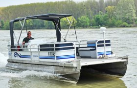 Ein kleines Motorboot f&auml;hrt auf einem Fluss, umgeben von B&auml;umen am Ufer.